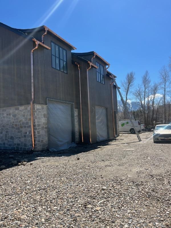 Multiple copper round downspouts on a mountain barn-style building with stone foundation.