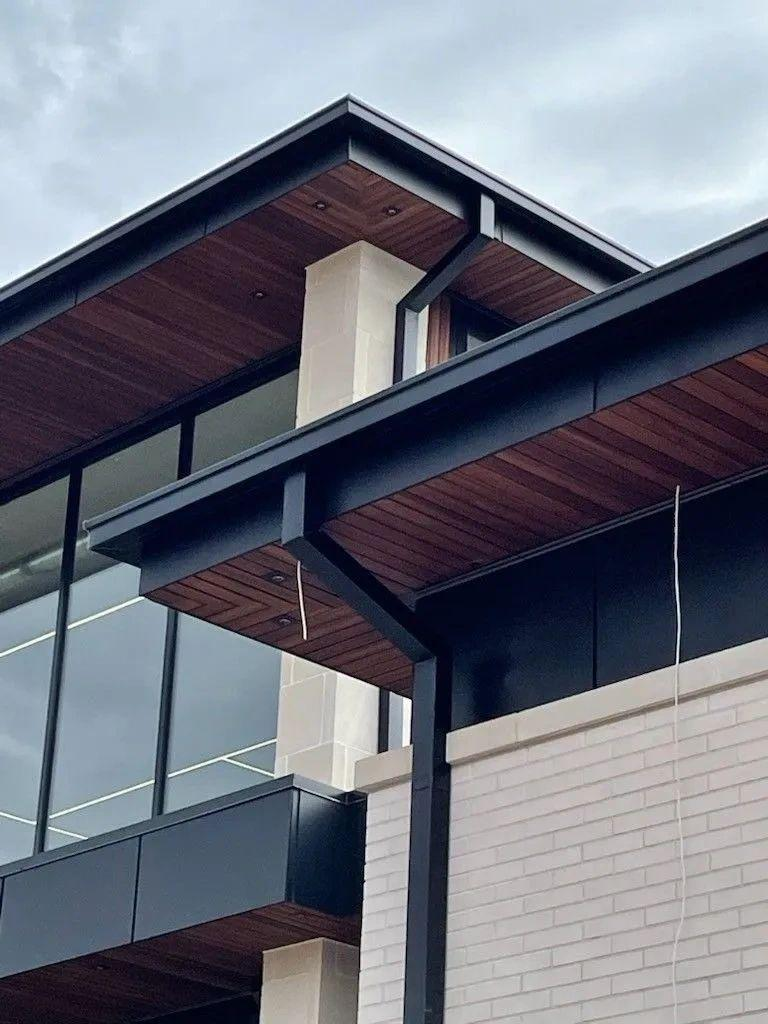 Architectural roofline with dark seamless box gutters, wood soffit, and stone column on a custom home.