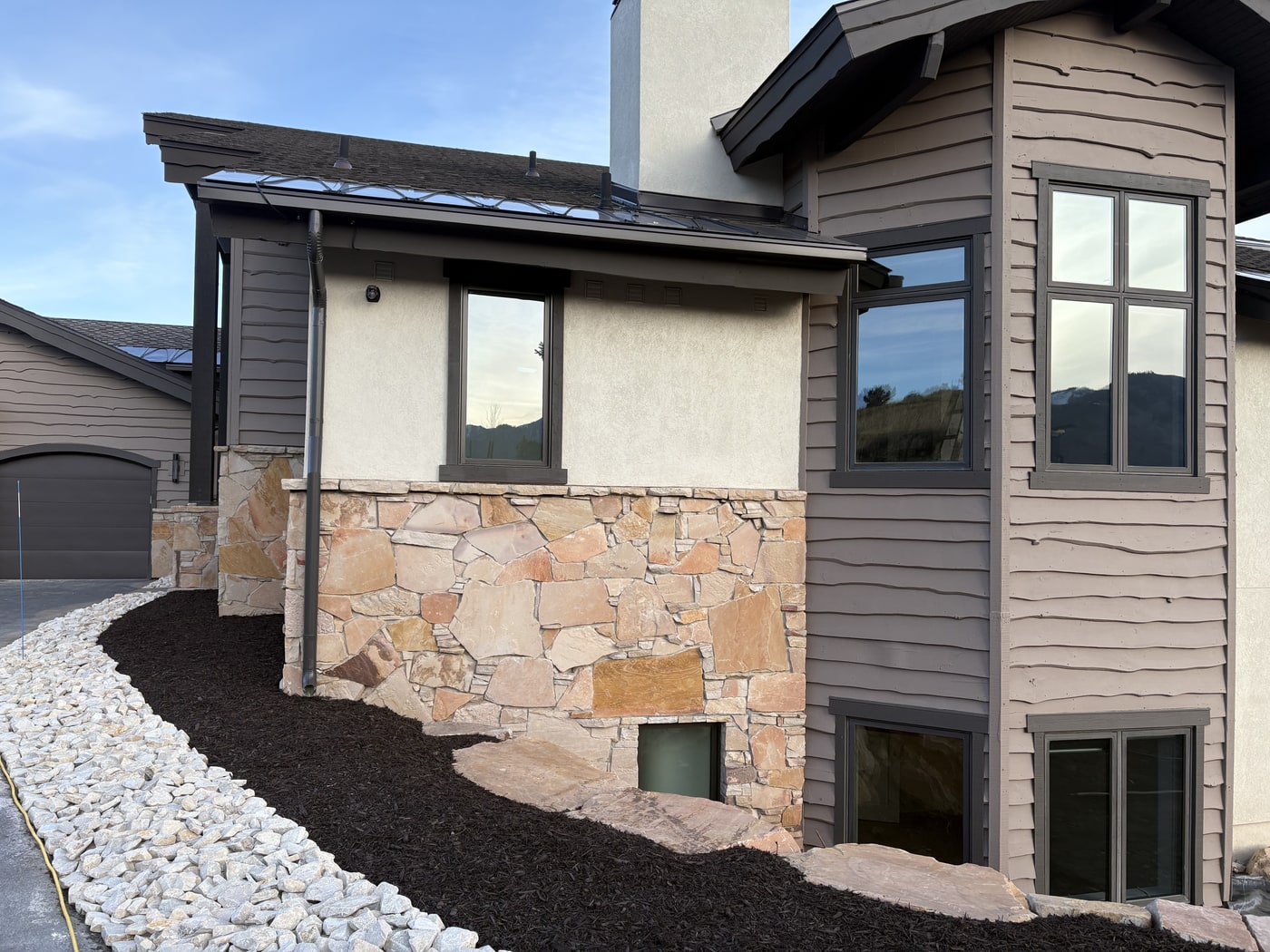 Dark charcoal K-style seamless gutters on a mountain home with stone base and brown siding.