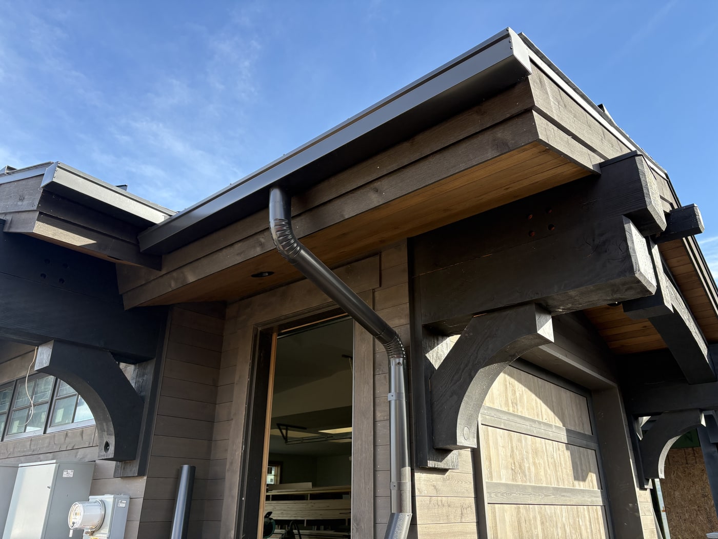 Dark K-style seamless gutters on a mountain home with exposed timber beams and wood soffit.